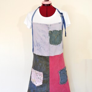 May include: Adult Large apron made from repurposed denim. The apron features a patchwork design with various denim washes and a pink panel. It has two pockets and the text "Apron #19".