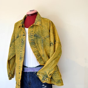 May include: A yellow acid wash denim jacket with a white t-shirt underneath and blue denim shorts. The jacket has a button-up front and long sleeves.