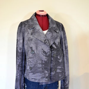 Può includere: Una giacca grigia tie-dye con chiusura a doppio petto e un motivo a righe. La giacca è su un manichino ed è abbinata a pantaloncini di jeans.