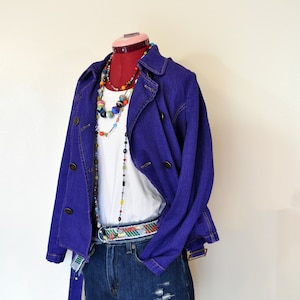 May include: A purple denim jacket with a white t-shirt and blue denim shorts. The jacket has a double breasted closure and a belt. The shorts have distressed details.