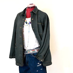 Op de afbeelding: Een donkergroen denim jack met een wit T-shirt en denim shorts. Het jack heeft een knoopsluiting aan de voorkant en twee zakken aan de voorkant. De shorts hebben een distressed look en een kleurrijke riem.