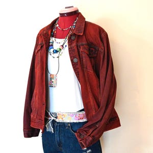 May include: A red denim jacket, white tank top, and denim shorts are displayed on a mannequin. The outfit is accessorized with a colorful beaded necklace and a patterned belt. The shorts have distressed details.