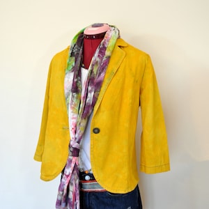 Könnte beinhalten: Ein gelber Leinenblazer mit einem Schal mit Blumendruck und Jeans-Shorts. Der Blazer hat einen einzigen Knopfverschluss und die Shorts haben Used-Look-Details.