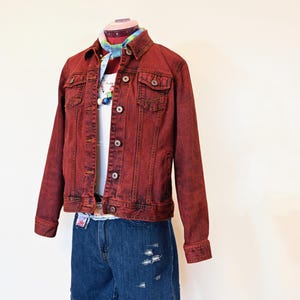 May include: A red denim jacket with a white shirt and blue denim shorts. The jacket has a button closure and two front pockets.