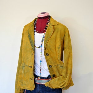May include: A yellow denim jacket with a white shirt and blue denim shorts. The jacket has a button closure and two pockets on the front. The shirt has a beaded necklace with colorful beads. The shorts have a belt with a colorful pattern.