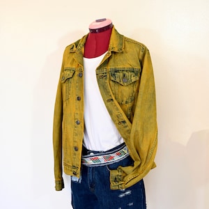 Op de afbeelding: Een geel denim jack met een wit T-shirt eronder en blauwe denim shorts met een kleurrijke riem.