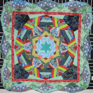 Puede incluir: Un edredón colorido, hecho a mano, con un diseño central de estrella. El edredón presenta una variedad de telas estampadas en tonos de azul, verde, rojo y amarillo. Los bordes están festoneados, agregando un toque decorativo.