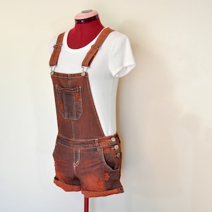 Puede incluir: Un short vaquero marrón con tirantes y una camiseta blanca en un maniquí.