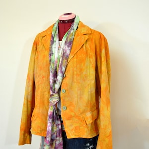 Puede incluir: Una chaqueta amarilla de teñido anudado con una bufanda de estampado floral y pantalones cortos de mezclilla.