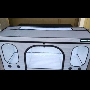 May include: A gray reptile enclosure with black trim and clear viewing windows. The enclosure has a zippered front door and the text "REPTILE TENTS" on the side. The top has a rectangular window.