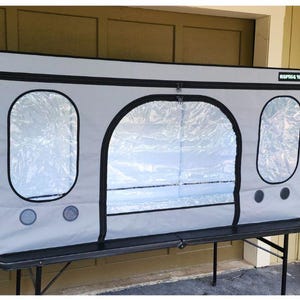 May include: A gray reptile enclosure with black trim and clear viewing windows. The enclosure has a zippered front door and circular ventilation ports. The text "Reptile Tents" is visible on the top right corner.