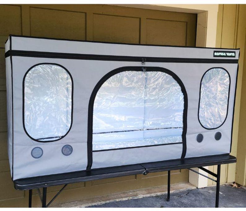 May include: A gray reptile enclosure with black trim and clear viewing windows. The enclosure has a zippered front door and circular ventilation ports. The text "Reptile Tents" is visible on the top right corner.