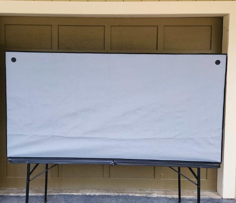 May include: A large, light gray screen stretched across a black folding table. The screen is rectangular with black trim and secured with black fasteners. The table has black metal legs.