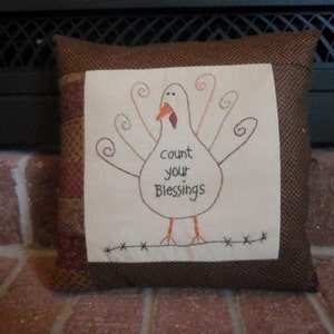 May include: A brown and white pillow with a stitched image of a turkey with the text "count your blessings".