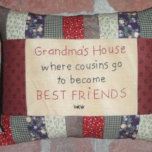 May include: A patchwork pillow with a beige background and red embroidered text that reads "Grandma's House where cousins go to become BEST FRIENDS xxx".