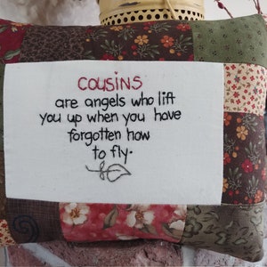 May include: A patchwork pillow with a white fabric panel featuring an embroidered quote: "Cousins are angels who lift you up when you have forgotten how to fly."