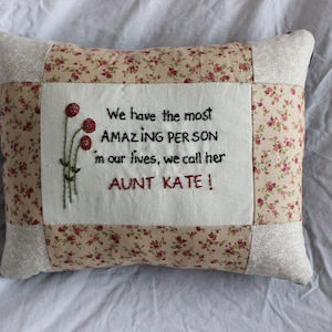 May include: A white pillow with a floral pattern and a message embroidered on it that reads "We have the most AMAZING PERSON in our lives, we call her AUNT KATE!"