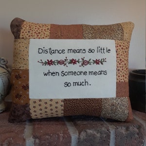 May include: A brown and beige patchwork pillow with the embroidered quote "Distance means so little when someone means so much."