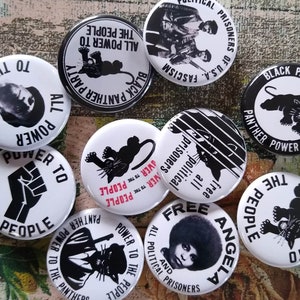 May include: A collection of white and black political buttons. The buttons feature text such as "Power to the People," "Black Panther Party," and images of a panther, a raised fist, and portraits. The buttons are arranged on a patterned surface.