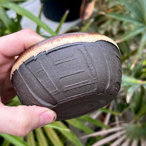 May include: A small, dark brown ceramic bowl with a light brown rim. The bowl has a textured, almost tire-like pattern on the outside.