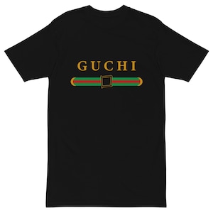 May include: Black short-sleeved t-shirt with the word "GUCCI" in gold letters and a green and red stripe with a gold buckle.