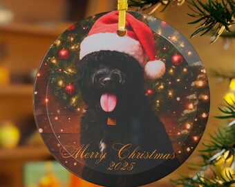 May include: Circular Christmas ornament with a black dog wearing a red Santa hat. The ornament is suspended by a gold ribbon and displays the text "Merry Christmas 2025". The background shows a decorated Christmas tree.