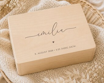 Könnte beinhalten: Eine rechteckige Erinnerungsbox aus hellem Holz mit dem Namen emilia in schwarzer Schreibschrift, einem kleinen Herzsymbol und dem Text 9. AUGUST 2026 • 3:23 3420G 54CM in einer schlichten serifenlosen Schrift auf der Oberseite.