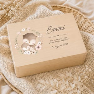 Könnte beinhalten: Eine rechteckige helle Holzbox mit einem aufgedruckten Bild von zwei Eulen in einem Blumenkranz. Der Text lautet Emmi, FÜR IMMER GELIEBT & UNENDLICH VERMISST und 2. August 2026, ergänzt durch ein kleines Herzsymbol auf der Holzoberfläche.