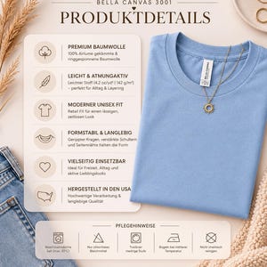 May include: A light blue Bella Canvas 3001 t-shirt with a round neck, featuring a gold necklace with a sun pendant. The shirt is displayed on a beige surface next to a pair of blue jeans. The image includes product details and care instructions.