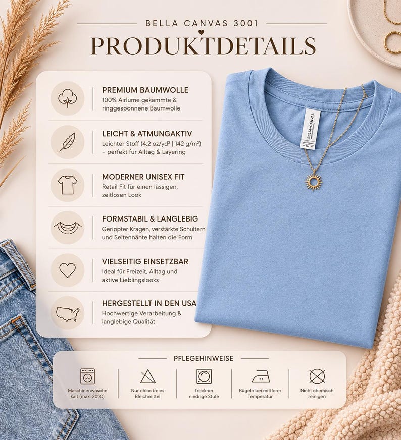 May include: A light blue Bella Canvas 3001 t-shirt with a round neck, featuring a gold necklace with a sun pendant. The shirt is displayed on a beige surface next to a pair of blue jeans. The image includes product details and care instructions.
