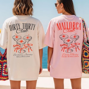 May include: Two oversized t-shirts, one cream and one light pink, featuring back graphics of three martini glasses with red cherries and ribbons. The cream shirt reads "DIRTY THIRTY Club Birthday Journey MALLORCA 2026" and the pink shirt reads "MALLORCA Club Dirty Thirty PALMA DE MALLORCA".