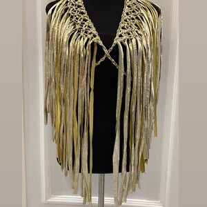 May include: A gold crocheted fringe vest with a V-neckline. The vest is made of thin, gold-colored strands of fabric that are woven together to create a delicate and intricate design. The fringe is long and flowing, adding a touch of bohemian style to the garment.