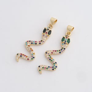 Peut inclure: Deux pendentifs dorés en forme de serpent. Chaque pendentif présente un corps serpentin incrusté de pierres précieuses colorées. Les têtes de serpent ont des yeux en pierres précieuses noires ou vertes. Les pendentifs sont conçus pour la bijouterie.