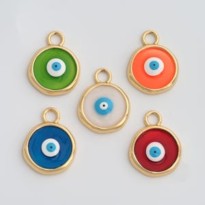 May include: Five colorful evil eye charms with gold-tone metal edging. The charms feature a central blue eye design on backgrounds of green, orange, white, blue, and red. Each charm has a small loop at the top for attaching to jewelry.