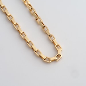 May include: A gold-coloured chain necklace with rectangular links. The chain is displayed on a white background. The links are connected in a repeating pattern, creating a simple yet elegant design. The necklace is a jewellery item.