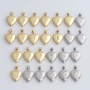 Op de afbeelding: Een verzameling hartvormige hangers, elk met een letter van het alfabet. De hangers zijn verkrijgbaar in goud- en zilverkleur, met een kleine lus voor een ketting. De letters zijn gegraveerd in een eenvoudig, elegant lettertype.