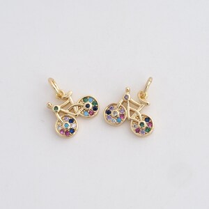 May include: Two gold-colored bicycle charms with colorful gemstone wheels. Each charm has a small loop at the top for attaching to a chain or bracelet. The gemstones are in shades of blue, green, pink, and purple.