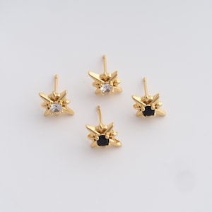 Puede incluir: Cuatro pendientes de botón dorados. Cada pendiente presenta un diseño de estrella con una gema central. Dos pendientes tienen gemas claras y dos tienen gemas negras. Los pendientes están sobre un fondo blanco.