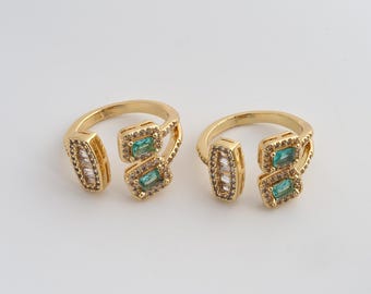 Puede incluir: Dos anillos dorados con un diseño abierto. Cada anillo presenta una piedra rectangular verde esmeralda y un grupo de piedras claras más pequeñas. Las bandas están adornadas con pequeños acentos brillantes, creando un diseño elegante y llamativo.