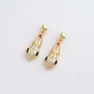Peut inclure: Deux pendentifs de collier en forme de serpent dorés. Chaque pendentif présente une tête de serpent ornée de cristaux transparents, d'accents verts et oranges. Les pendentifs ont une boucle en haut pour une chaîne.