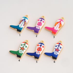 May include: Six metal cowboy boot charms with gold-toned edges and enamel fill. Each charm features a white upper section with distinct colorful patterns including butterflies, roses, and stars, paired with solid-colored feet numbered one through six.