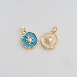 Peut inclure: Deux pendentifs dorés avec des motifs de tortues. L'un a un fond bleu clair, l'autre un fond rose clair. Les deux pendentifs ont une tortue dorée au centre et une boucle dorée en haut pour les suspendre.
