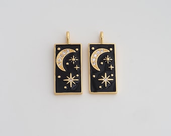May include: Two gold-toned rectangular pendants with a black enamel background. Each pendant features a crescent moon with clear crystals and starburst and dot designs. The pendants have a gold loop at the top for hanging.