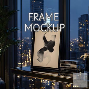 May include: A black framed picture with an abstract black and white design on a beige background. The picture is on a black glass table in front of a window with a city view at night. The text "FRAME MOCKUP" is in white letters at the top of the image.