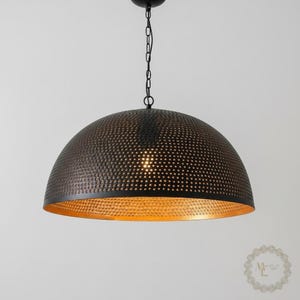 May include: A dome-shaped pendant light fixture featuring a matte black exterior with a perforated pattern and a metallic gold interior finish. The lamp is suspended by a black metal chain and includes a central light bulb socket.