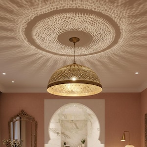 Puede incluir: Una lámpara colgante decorativa con una pantalla dorada estampada cuelga del techo. La luz proyecta un diseño estampado en el techo. La habitación tiene una paleta de colores cálidos con un espejo y un cabecero tallado.