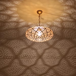 May include: A gold-toned, round, hanging light fixture with a geometric pattern. The light fixture casts a patterned shadow on the ceiling.