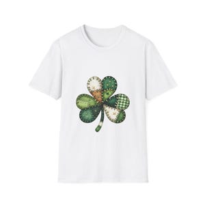 Könnte beinhalten: Weißes T-Shirt mit einem großen Kleeblatt-Design in Patchwork-Optik. Das Kleeblatt besteht aus verschiedenen grünen und beigefarbenen Stoffstücken, darunter ein kariertes Muster. Ein Stiel erstreckt sich nach unten.