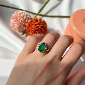 Puede incluir: Un anillo de oro con una piedra preciosa verde en forma de lágrima. El anillo está en el dedo de una persona.