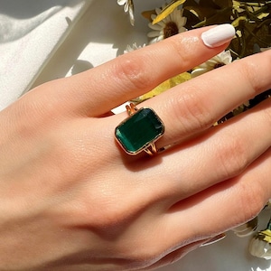 May include: A gold ring with a large, square, emerald green gemstone.